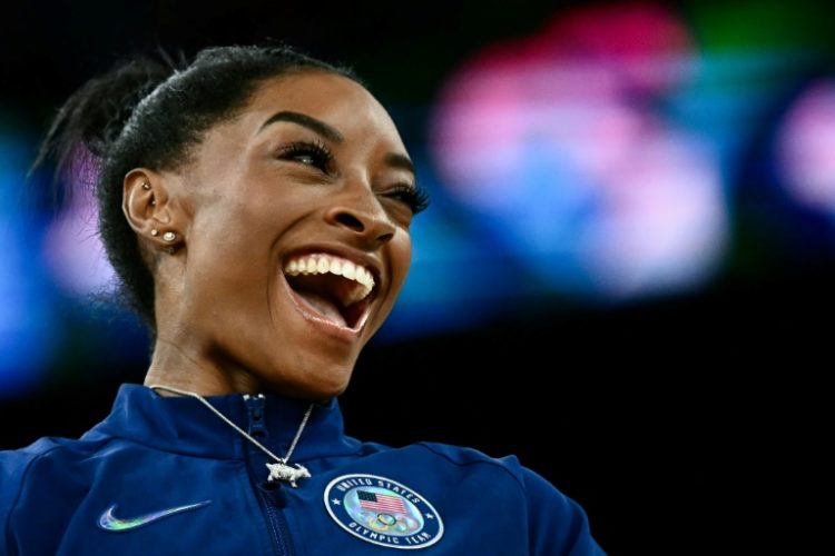 Simone Biles poses with her goat necklace during the podium ceremony after winning the women's gymnastics all-around title at the Paris Olympics. ©AFP