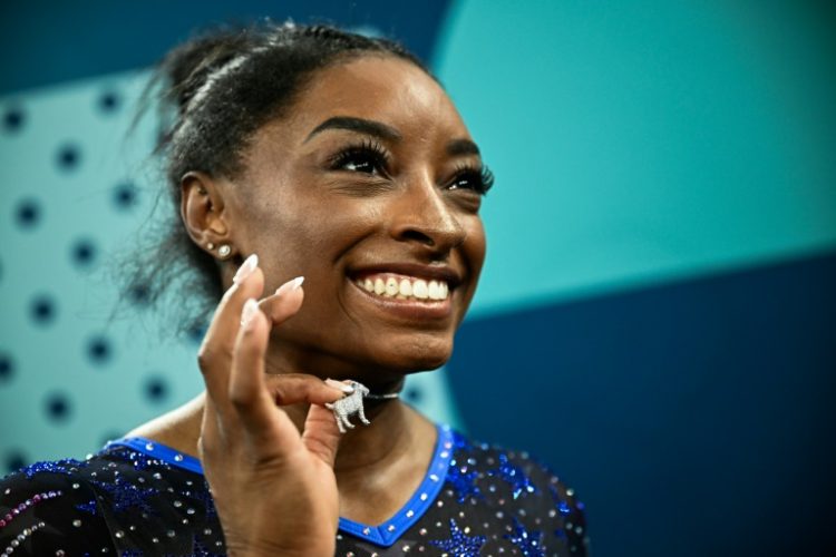 Simone Biles poses with her goat necklace after winning the women's gymnastics all-around title at the Paris Olympics. ©AFP